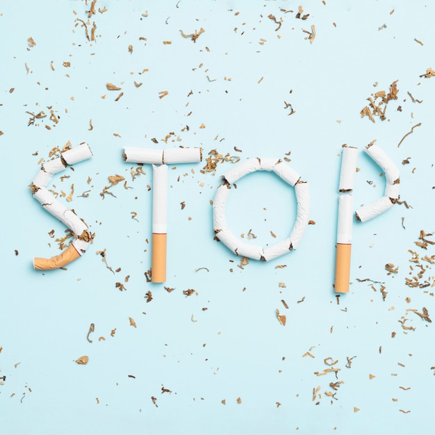Smetta di fumare il testo fatto con la sigaretta e il tabacco rotti su priorità bassa blu