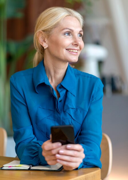 Smiley donna più anziana tenendo lo smartphone mentre si lavora