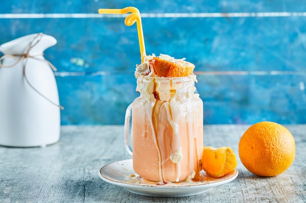 Smoothie all'arancia con panna, paglia e fettine d'arancia in superficie in marmo