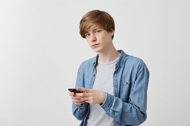 SMS di moda giovane su smart phone alla fidanzata, stand, gode di una connessione internet gratuita. Lo studente maschio in camicia di jeans scrive il messaggio ai suoi genitori, sembra.