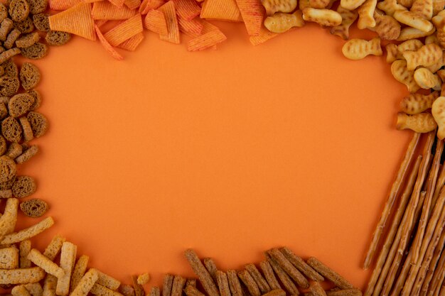 Snack vista dall'alto con copia spazio paprika chips cracker bastoncini duri e mini brezel su sfondo arancione
