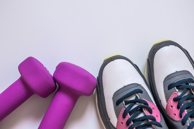 Sneakers e manubri fitness su uno sfondo bianco. Strumenti diversi per lo sport. Concetto sano stile di vita, sport e dieta. Equipaggiamento sportivo. Copia spazio. Pianta piatta di accessori fitness e allenamento