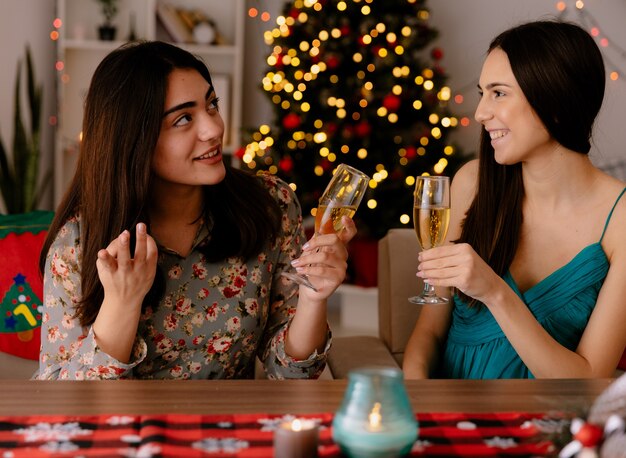 soddisfatte ragazze carine tengono bicchieri di champagne seduti a tavola e godersi il periodo natalizio a casa