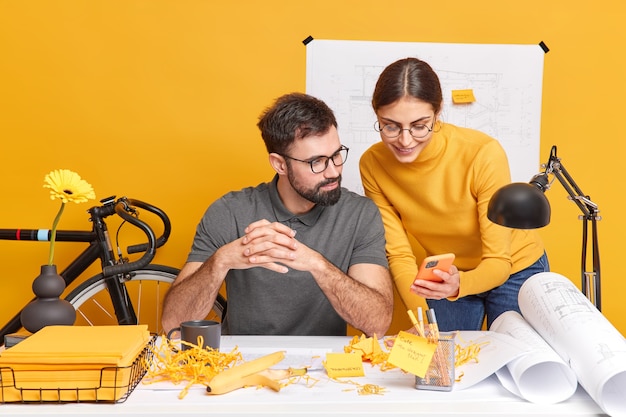 Soddisfatti giovani professionisti donna e uomo impiegati collaborano insieme durante il lavoro di squadra su progetti ricerca di idee in internet concentrati sul cellulare moderno discutono idee per progetto