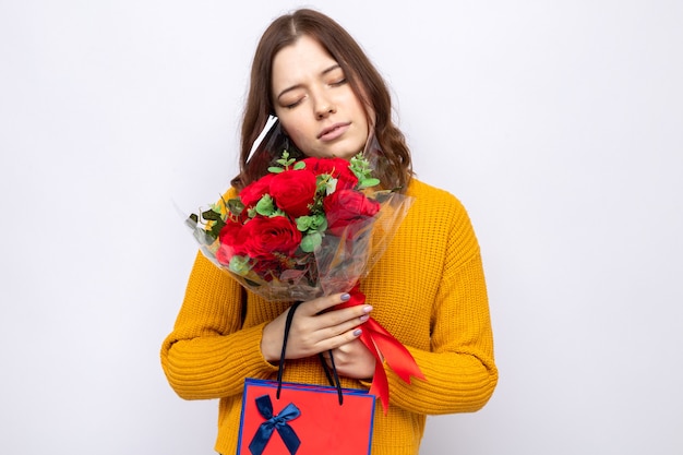 Soddisfatto degli occhi chiusi bella ragazza che tiene in mano una borsa regalo con bouquet