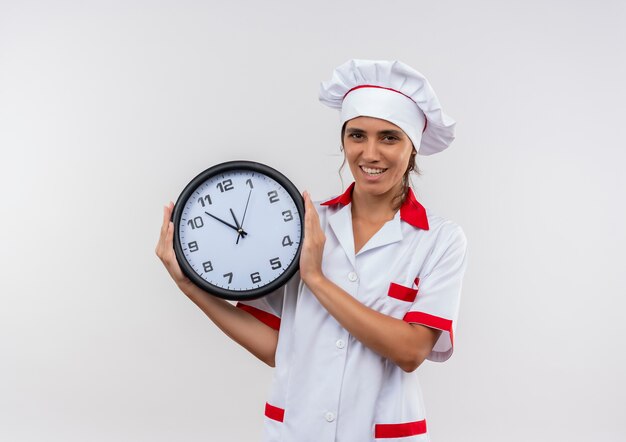 Soddisfatto giovane cuoco femminile che indossa lo chef uniforme tenendo l'orologio da parete con lo spazio della copia