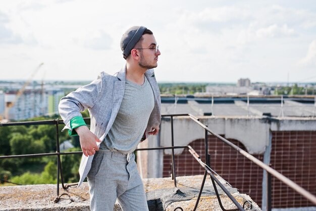 Sognatore elegante uomo macho in abito grigio cappello e occhiali posato sul tetto