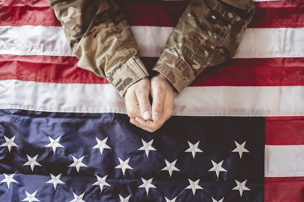 Soldato americano in lutto e in preghiera con la bandiera americana davanti