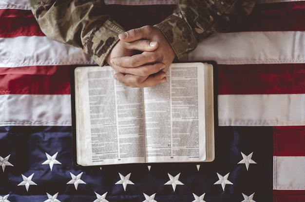Soldato americano in lutto e in preghiera con la bandiera americana e la Bibbia davanti a sé