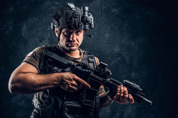 Soldato brutale della Federazione Russa che indossa un'armatura e un casco con una visione notturna in posa con un fucile d'assalto. Foto dello studio contro una parete strutturata scura