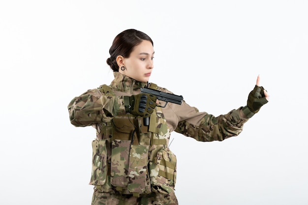 Soldato femminile di vista frontale in camuffamento con la pistola sulla parete bianca