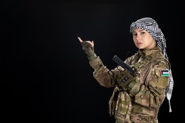 Soldato femminile in uniforme militare con pistola sul muro nero