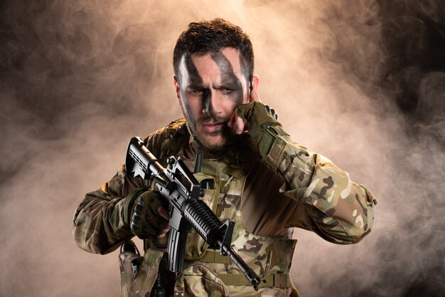 Soldato in mimetica con mitragliatrice sul muro scuro e fumoso