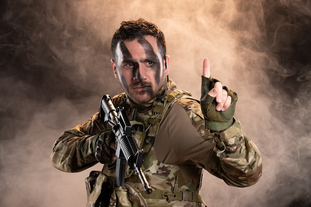 Soldato in mimetica con mitragliatrice sul muro scuro e fumoso