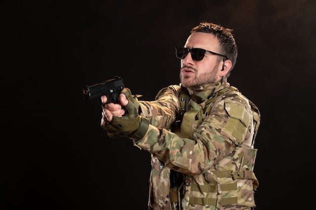 Soldato maschio in mimetica con pistola sul muro nero