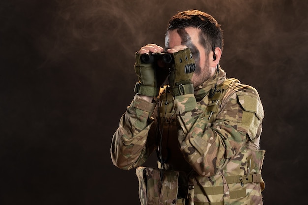 Soldato maschio in uniforme militare con binocolo sul muro scuro