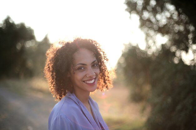 Sole che splende su una donna con i capelli ricci circondata da alberi ed erba