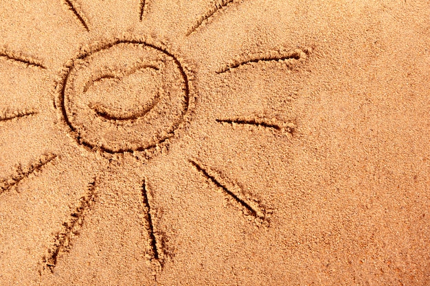 sole sorridente disegnato su una spiaggia di sabbia