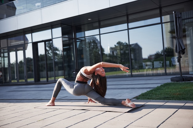 Soleggiata mattina d'estate. Giovane donna atletica che fa verticale sulla via del parco della città fra le costruzioni urbane moderne. Esercizio all'aperto stile di vita sano