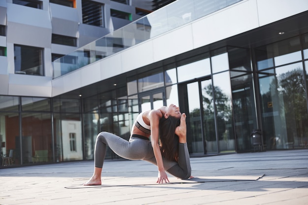 Soleggiata mattina d'estate. Giovane donna atletica che fa verticale sulla via del parco della città fra le costruzioni urbane moderne. Esercizio all'aperto stile di vita sano