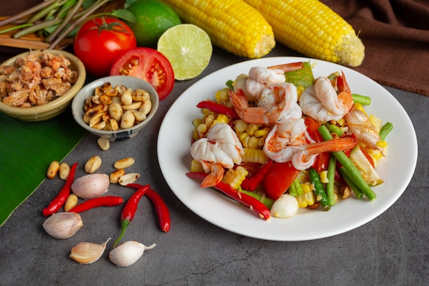 Som Tum con mais e gamberetti, servito con spaghetti di riso e insalata verde Decorato con ingredienti alimentari tailandesi.