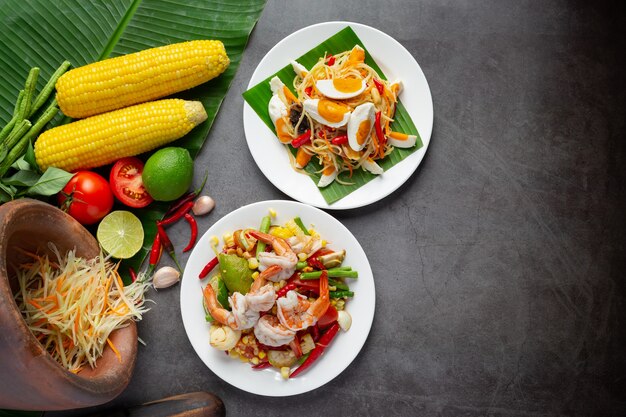 Som Tum con mais e gamberetti, servito con spaghetti di riso e insalata verde Decorato con ingredienti alimentari tailandesi.