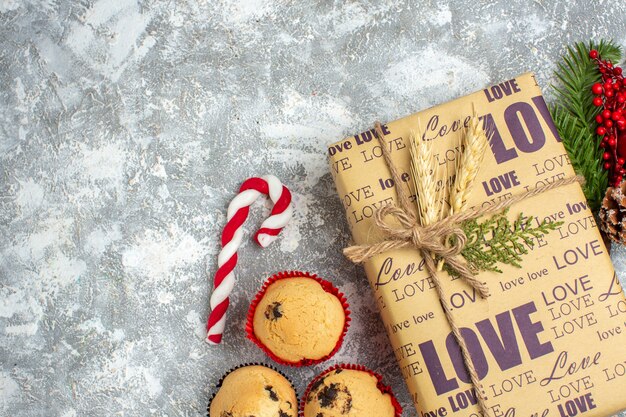 Sopra la vista del bellissimo regalo di Natale confezionato con iscrizione d'amore piccoli cupcakes caramelle e rami di abete accessori per la decorazione cono di conifere sul lato sinistro sulla superficie del ghiaccio