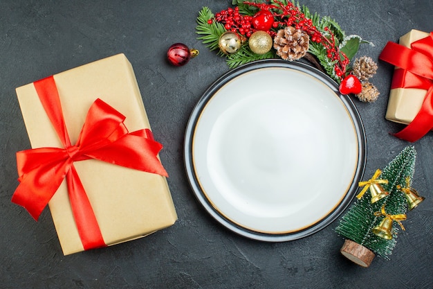 Sopra la vista del contenitore di regalo del cono di conifera dei rami di abete dell'albero di Natale del piatto della cena con il nastro rosso su fondo nero