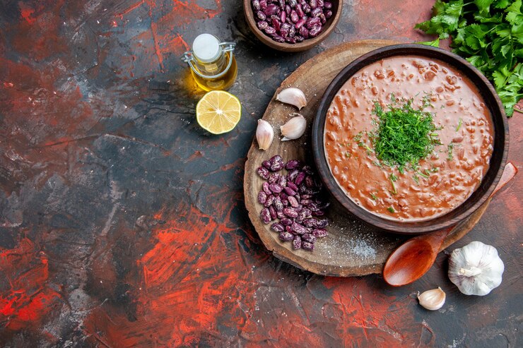 Foto gratuito sopra la vista del cucchiaio di aglio di fagioli di sapone di pomodoro sul tagliere di legno e bottiglia di olio verde limone