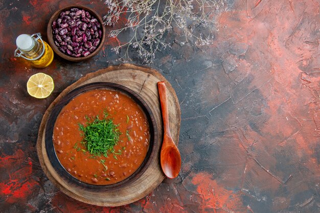 Sopra la vista della classica zuppa di pomodoro in una ciotola marrone bottiglia di olio fagioli e cucchiaio sul tavolo di colori misti