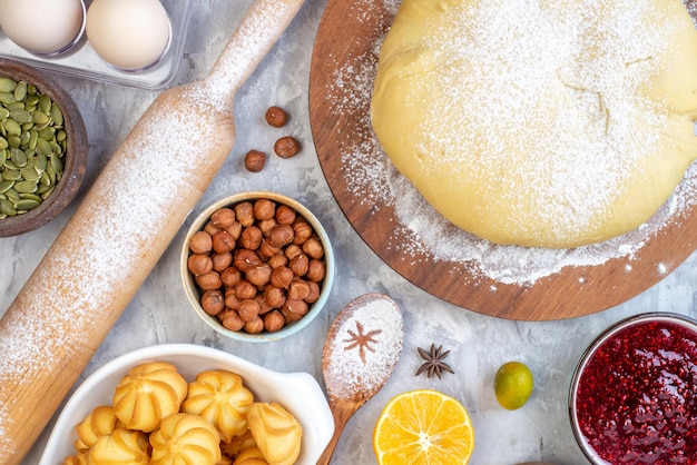 Sopra la vista della farina cruda della pasticceria sulla tavola rotonda biscotti alle nocciole della marmellata di frutta fresca su fondo bianco macchiato