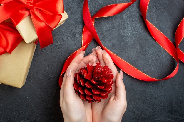 Sopra la vista della mano che tiene un cono di conifere e bel regalo su sfondo scuro