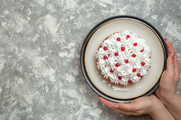 Sopra la vista della mano che tiene un piatto con una deliziosa torta cremosa decorata con frutta