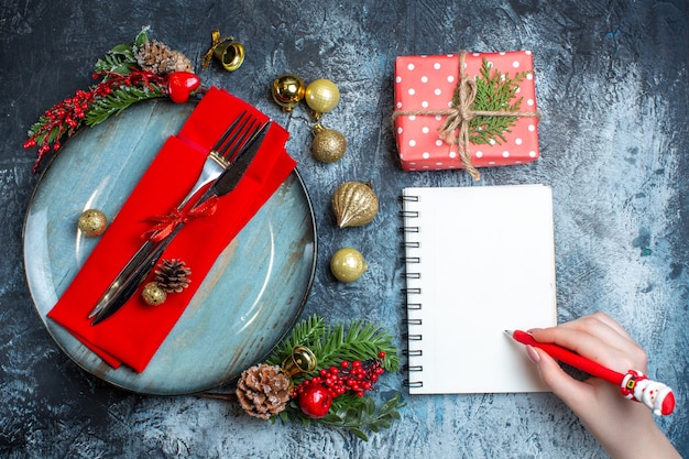 Sopra la vista della mano che tiene una penna su un quaderno a spirale e una confezione regalo accanto al set di posate