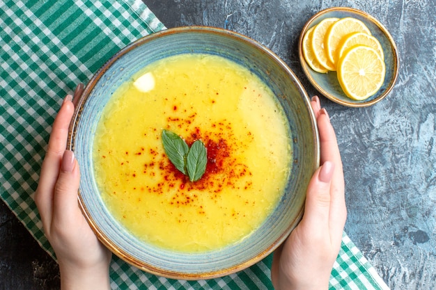 Sopra la vista della mano che tiene una pentola blu con una gustosa zuppa servita con menta e pepe