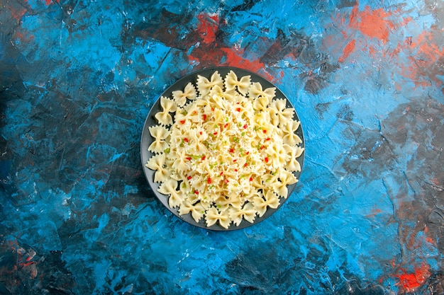 Sopra la vista della pasta italiana cruda del farfalle con le verdure su fondo blu