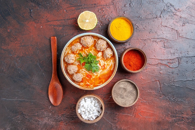 Sopra la vista della zuppa di polpette con noodles in una ciotola marrone cucchiaio di limone e spezie diverse su sfondo scuro