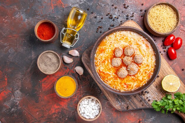 Sopra la vista della zuppa di polpette con tagliatelle pasta cruda tagliere limone un mazzetto di pomodori verdi spezie diverse sul tavolo scuro