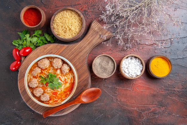 Sopra la vista della zuppa di polpette di pomodoro con tagliatelle in una ciotola marrone e diverse spezie olio bottiglia cipolla aglio su sfondo scuro fotografia stock