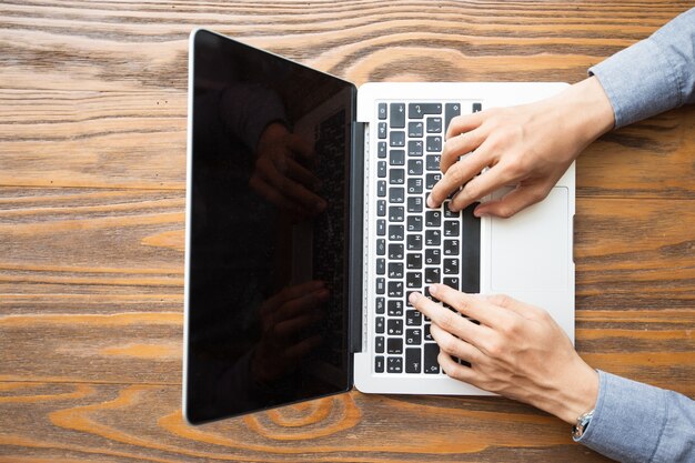 Sopra la vista delle mani maschili digitando sul computer portatile a tavola