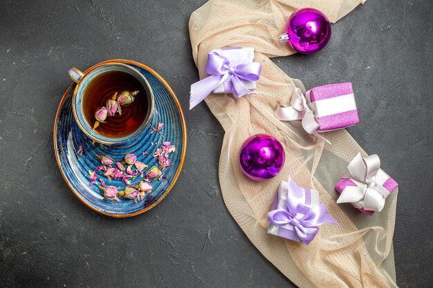 Sopra la vista di accessori per la decorazione di regali colorati per il nuovo anno su un asciugamano di colore nudo e una tazza di tè su sfondo nero