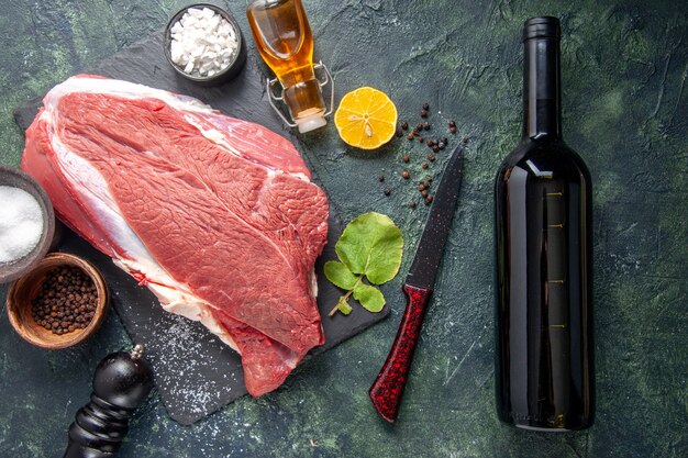 Sopra la vista di carne rossa cruda fresca su vassoio nero pepe limone olio martello in legno bottiglia di vino su sfondo di colore scuro