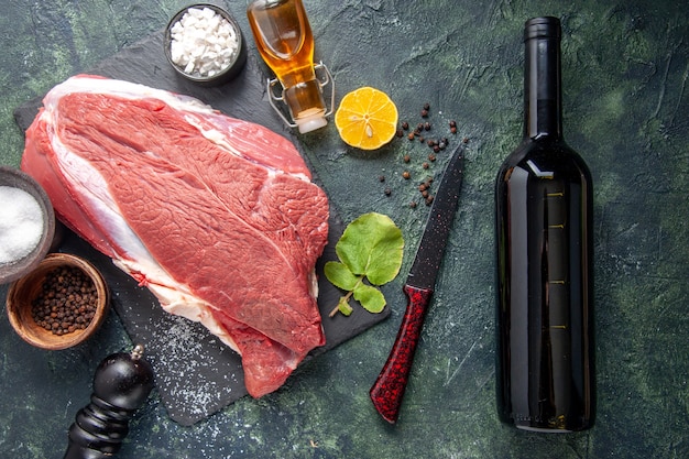 Sopra la vista di carne rossa cruda fresca su vassoio nero pepe limone olio martello in legno bottiglia di vino su sfondo di colore scuro