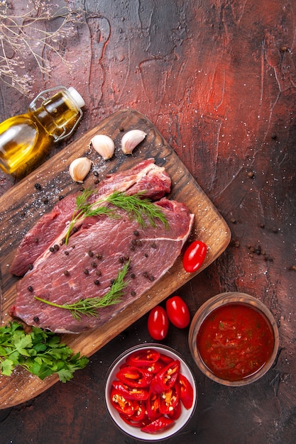 Sopra la vista di carne rossa su tagliere di legno e ketchup di bottiglia di olio caduto pepe verde tritato di aglio su sfondo scuro