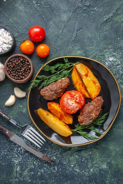 Sopra la vista di deliziose cotolette di carne al forno con patate e pomodori su un piatto nero set di posate spezie garlics tomato