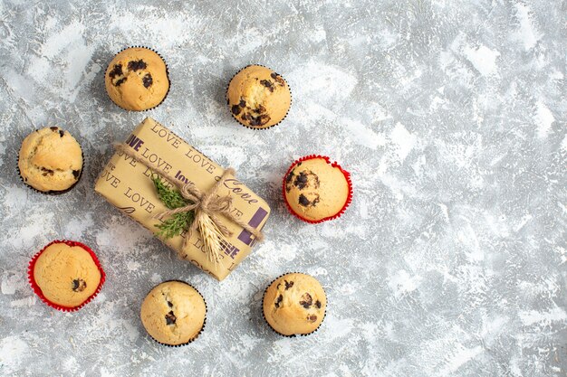 Sopra la vista di deliziosi piccoli cupcakes con cioccolato intorno al regalo con iscrizione d'amore sul lato sinistro sulla superficie del ghiaccio ice