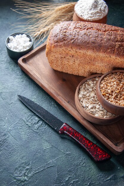 Sopra la vista di farina di fette di pane nero in una ciotola su tavola di legno e punte di coltello farina d'avena cruda di grano sul lato sinistro su sfondo invecchiato di colori misti