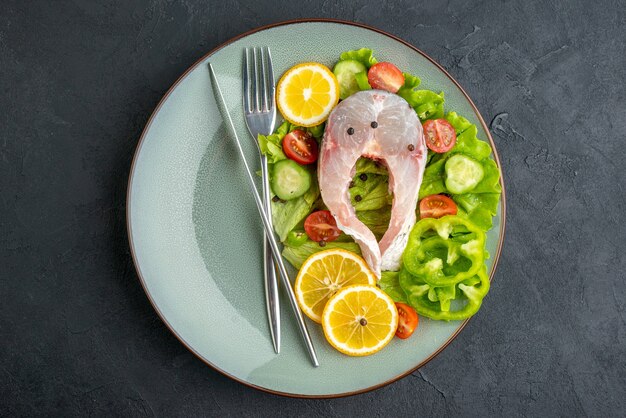 Sopra la vista di pesce crudo e verdure fresche fette di limone e posate su un piatto grigio su superficie nera con spazio libero free