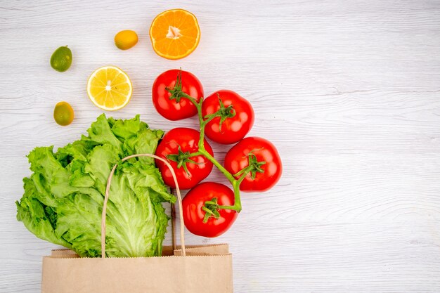 Sopra la vista di pomodori freschi con gambo e kumquat al limone verde sul lato destro su sfondo bianco