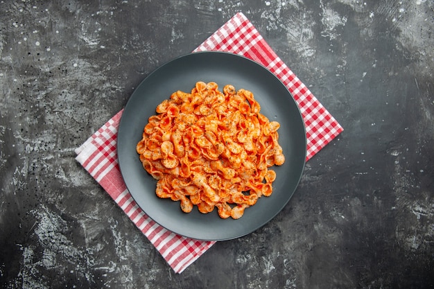 Sopra la vista di un delizioso pasto di pasta su un piatto nero per cena su un asciugamano spogliato rosso su sfondo scuro